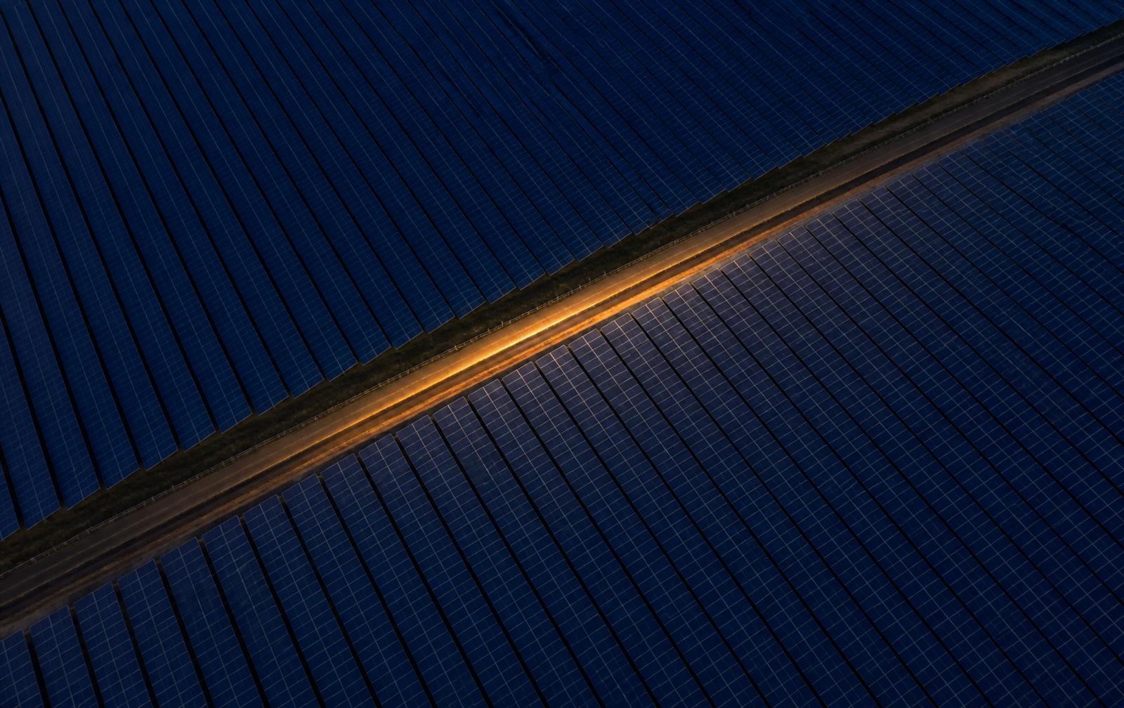 Overhead view of two adjoining solar array fields meeting along a shared boundary road at dusk