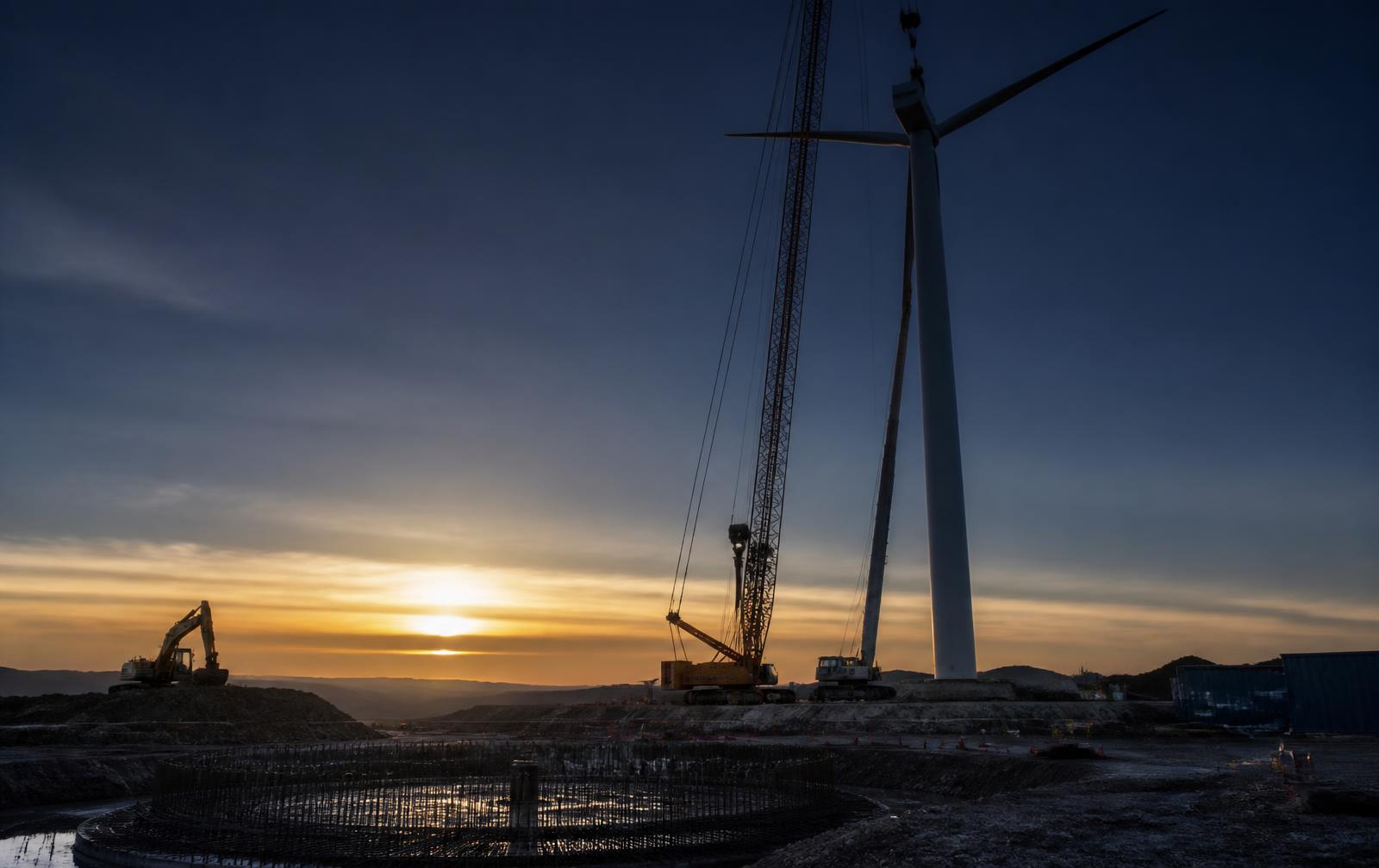 Wind turbine erection and earthworks on a renewable construction site at dawn