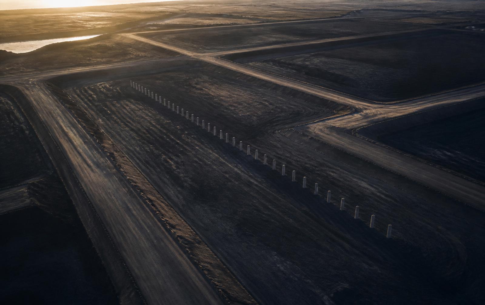 Aerial view at dawn of an early-stage project site with graded access roads and a line of foundation piles