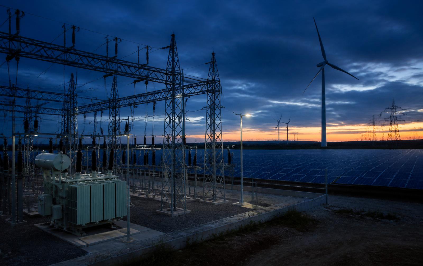 High-voltage substation with solar and wind generation at blue hour.