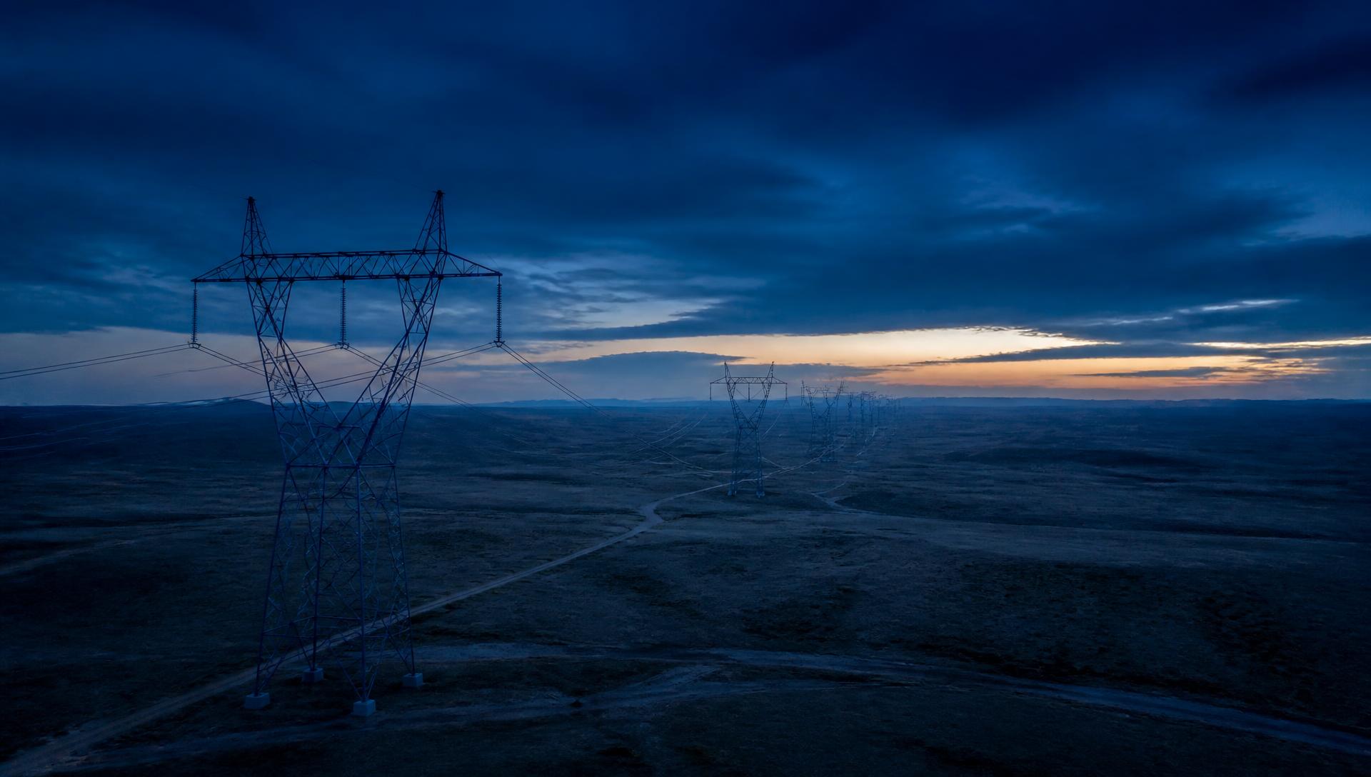 High-voltage transmission corridor crossing open terrain at blue hour.